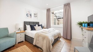 Une chambre moderne comprenant un lit, des tables de chevet, une chaise, un bureau et une fenêtre avec des rideaux.