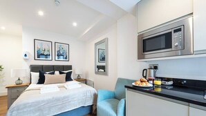 A modern hotel room with a bed, bedside tables, a small kitchenette, and a microwave. - PBC | Studio Apartment in Bayswater (LS2) (London)
