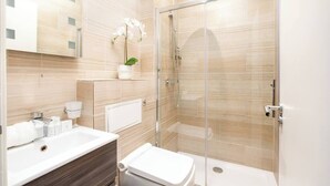 A modern bathroom with a glass shower enclosure, a white sink, and a toilet. - PBC | Studio Apartment in Bayswater (LS2) (London)
