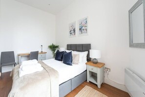 Una habitación de hotel moderna con cama, mesita de noche, silla, escritorio y una obra de arte en la pared.