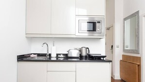 Une cuisine compacte avec des meubles blancs, un four à micro-ondes en acier inoxydable, une bouilloire et un grille-pain.