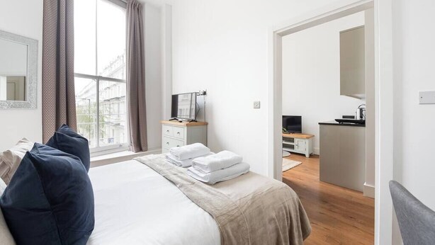 Une chambre d’hôtel moderne dotée d’un grand lit, d’un bureau avec un ordinateur, d’une télévision et offrant une vue sur la ville par la fenêtre.