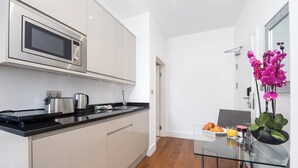 A modern kitchen with a microwave, coffee maker, and toaster. There is a dining area with a glass table and chairs, and a small plant on the table. - PBC | Modern Studio in Bayswater LS10 (London)