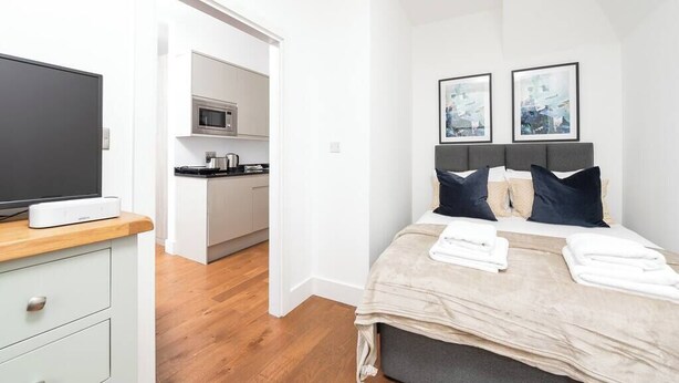 A modern hotel room with a bed, a TV, a kitchenette, and artwork on the wall. - PBC | Modern Studio in Bayswater LS10 (London)