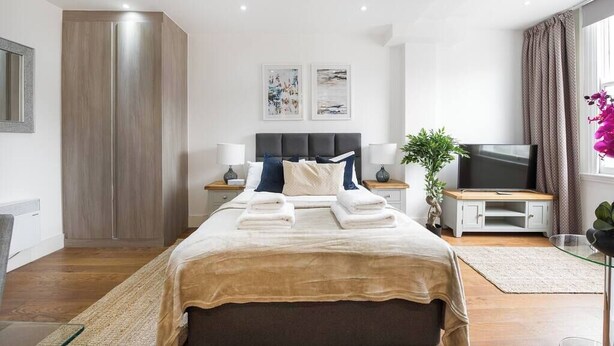 Moderni hotellihuone, jossa on suuri sänky, taulutelevisio, vaatekaappi ja kaksi kehystettyä taideteosta seinällä.