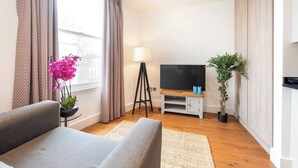 Ein modernes Wohnzimmer mit einer Couch, einem Fernseher auf einem Schrank, einer Lampe und einem Topfpflanzen.
