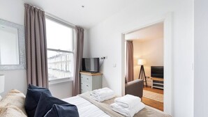 Ein Hotelzimmer mit einem Bett, einem Fernseher, einem Schreibtisch und einem Vorhangfenster.