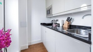 Una cocina moderna con armarios blancos, encimera negra, pileta de acero inoxidable y un microondas.