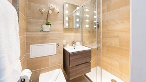 Un baño moderno con cabina de ducha de vidrio, tocador blanco y una orquídea en maceta en la pared.