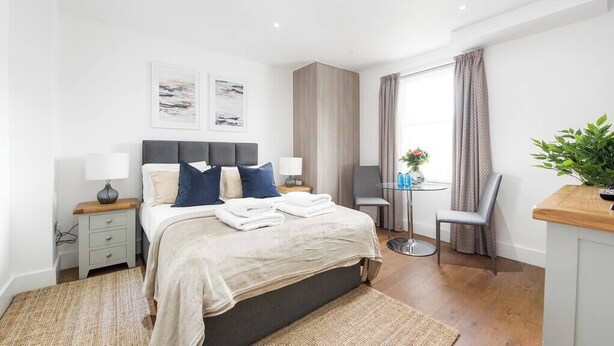 Un dormitorio moderno con cama, mesitas de noche, una pequeña mesa redonda y una silla.