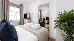 Una habitación de hotel con una cama, un escritorio con una computadora, un televisor y una planta.