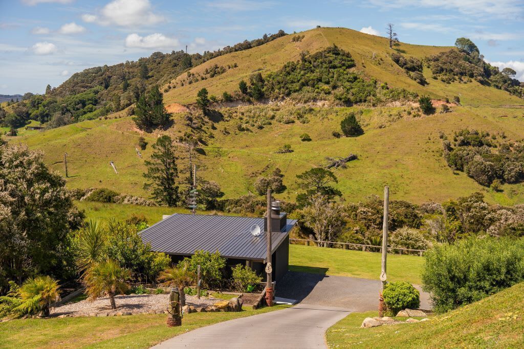 A rural landscape with a house on a hill, a paved driveway, and surrounding greenery.