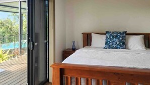 A bedroom with a wooden bed, a nightstand, and a large sliding glass door leading to a balcony. - Daintree Getaway is a secluded holiday home nestled in a private oasis (Lower Daintree)