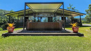 A modern house with a glass facade, a covered porch, and a well-maintained lawn. - Daintree Getaway is a secluded holiday home nestled in a private oasis (Lower Daintree)