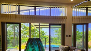 A modern living room with a large glass door leading to a balcony, a sofa with cushions, and a decorative glass vase. - Daintree Getaway is a secluded holiday home nestled in a private oasis (Lower Daintree)