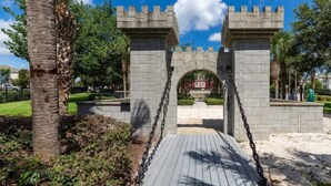 A stone archway with a wooden walkway leading through it, surrounded by greenery and palm trees. - Comfy 3-bedroom condo/Windsor Hills Resort/gated/Waterpark/close to Disney (Kissimmee)