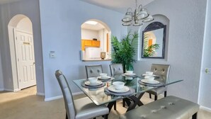 A dining area with a glass table set for six, surrounded by grey upholstered chairs. - Comfy 3-bedroom condo/Windsor Hills Resort/gated/Waterpark/close to Disney (Kissimmee)