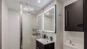 A modern bathroom with a glass shower enclosure, a vanity with a mirror, and a toilet. - Spacious loft Luxembourg Garden (Paris)