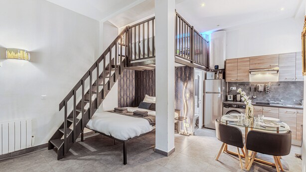 A modern apartment with a staircase leading to a loft bedroom, a kitchen with stainless steel appliances, and a dining area with a glass table. - Spacious loft Luxembourg Garden (Paris)