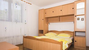 Un dormitorio con cama de madera, mesita de noche, armario y ventana con cortinas.