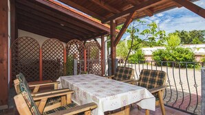 Un patio techado con una mesa y sillas, una cerca de madera, y vistas a zonas verdes y edificios.