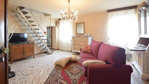 A living room with a staircase, a chandelier, a television, a sofa, and a dining area.