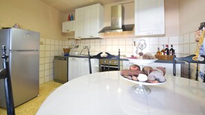 A kitchen with white cabinets, a stainless steel refrigerator, and a dining table with a fruit bowl.