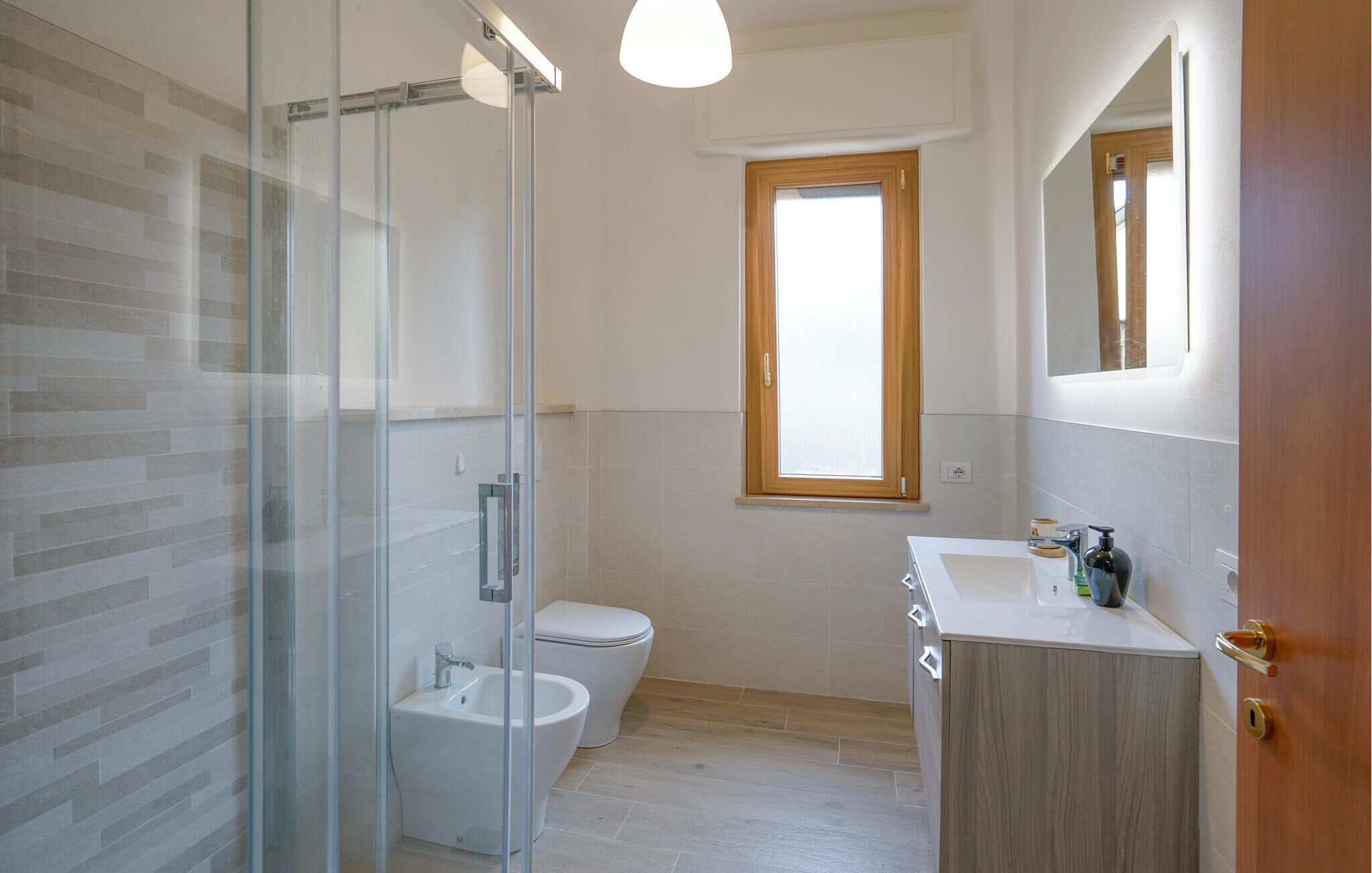 Een moderne badkamer met een glazen douchecabine, een toilet en een wastafel met een houten kastje.
