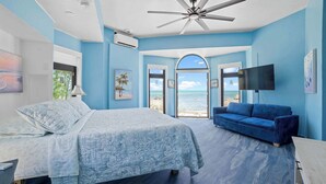 A bedroom with a bed, a blue sofa, a TV, and a view of the beach.