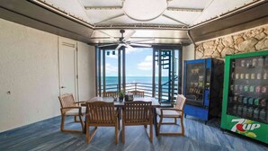 A dining area with a table and chairs, a ceiling fan, a 7UP vending machine, and a view of the ocean. - Star Room Barnacle Resort (Big Pine Key)