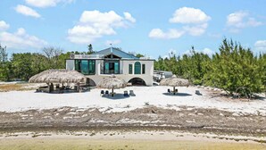 A beachfront property with a white building, thatched umbrellas, and clear water. - Treehouse Private Village Barnacle Resort (Big Pine Key)