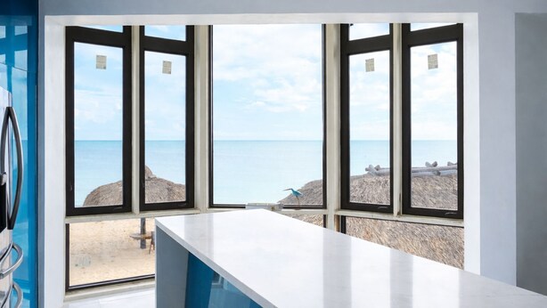 A room with a large window overlooking a beach, a white countertop, and a blue wall. - Treehouse Private Village Barnacle Resort (Big Pine Key)