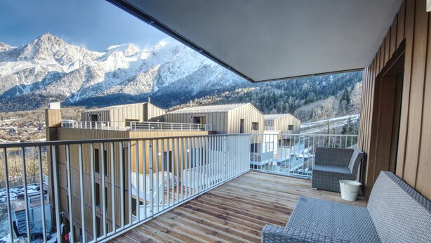 A balcony with a wooden deck, wicker furniture, and a view of snow-capped mountains.
