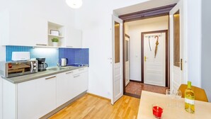 A compact kitchen with white cabinets, a coffee machine, and a toaster. There is a dining area with a table, two wine glasses, and a candle. - Central & Parking Assistance (Prague)