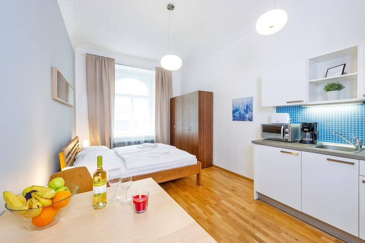 A hotel room with a bed, a small kitchen area with a microwave, a coffee maker, and a fruit bowl on the table.