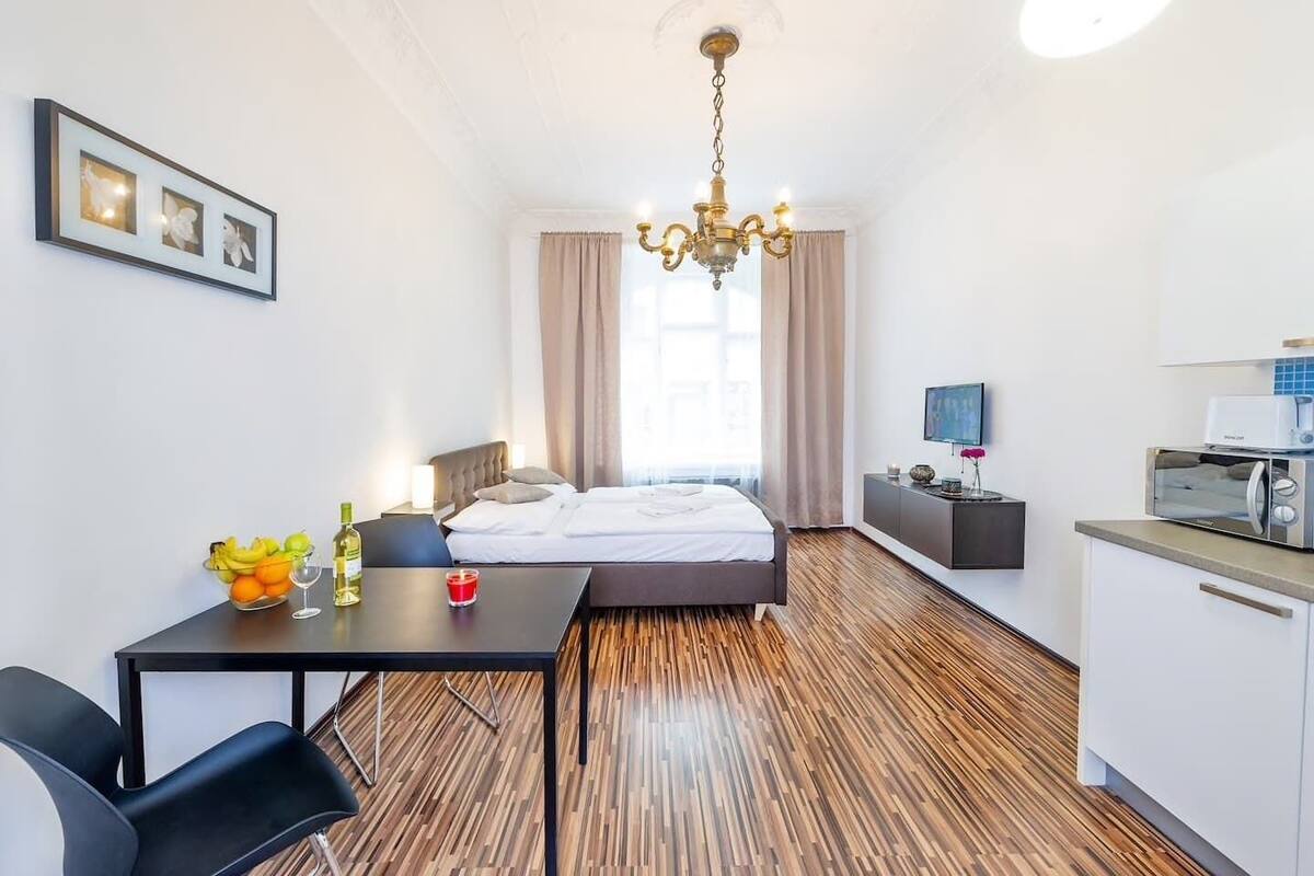 A modern hotel room with a bed, bedside table, and a small kitchenette.