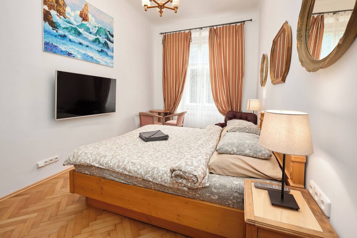 A bedroom with a bed, a TV, a bedside table, a lamp, and a painting of waves on the wall.