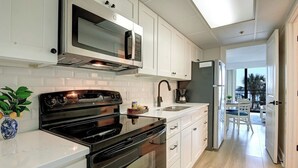A modern kitchen with white cabinetry, a black stove, a microwave, and a coffee maker.