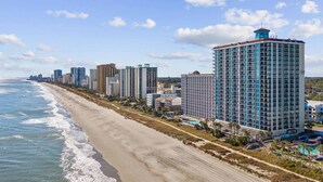 A beachfront hotel with a long, sandy beach and ocean view, modern architecture, and a pool area.