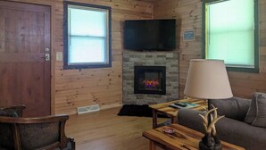 A cozy cabin interior with a fireplace, wooden walls, a television, and a comfortable seating area. - Cozy Cottage-Devil`s Bathtub/Nat Tunnel (Duffield)