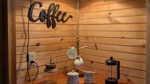 A wooden interior with a wall-mounted sign reading "Coffee," a hanging light fixture, and a wooden countertop with a coffee maker, mug, and thermos. - Cozy Cottage-Devil`s Bathtub/Nat Tunnel (Duffield)