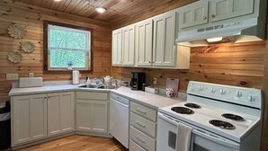 A compact kitchen with white cabinets, a stove, and a window with blinds. - Cozy Cottage-Devil`s Bathtub/Nat Tunnel (Duffield)