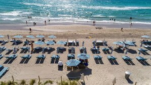 Una playa con filas de tumbonas y sombrillas a rayas, una orilla arenosa y el océano al fondo.