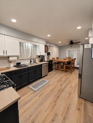A modern kitchen with a dining area, wooden flooring, and a ceiling fan.