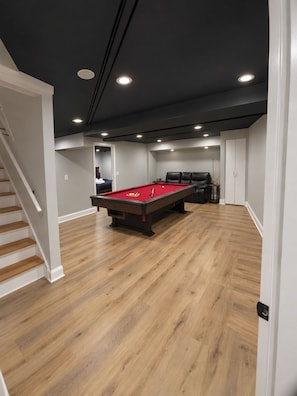 A room with a pool table, a staircase, and a door leading to another room.