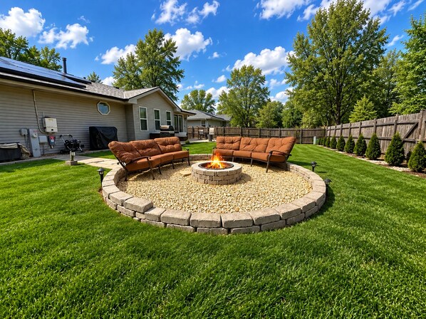 A circular outdoor seating area with a fire pit, surrounded by a stone wall, in a residential backyard.