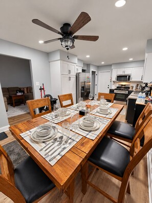 A modern kitchen with white cabinetry, a stainless steel refrigerator, and a dining area set for six with wooden chairs and a table.