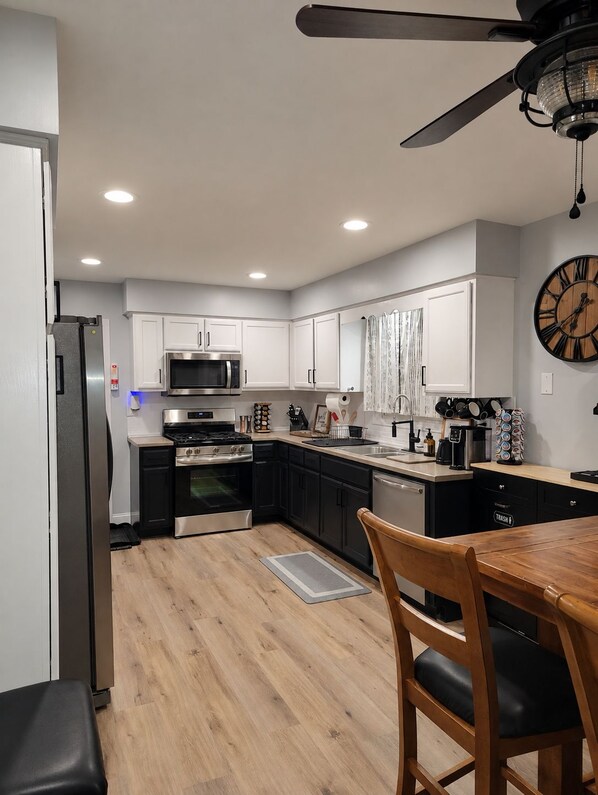 Una cocina moderna con armarios blancos, encimera negra, electrodomésticos de acero inoxidable y un comedor con mesa y sillas de madera.