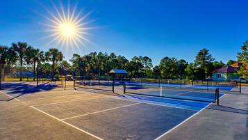 Un court de tennis avec un filet, entouré d’arbres et sous un ciel dégagé.