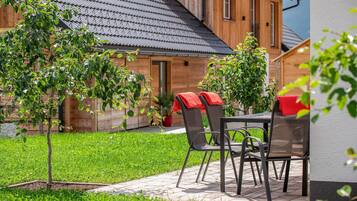 Ein Sitzbereich im Freien mit Tisch und Stühlen, ein Holzgebäude im Hintergrund und eine Rasenfläche.